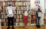 Zdjecie laureatow komkursu z dyplomami w tle regal biblioteczny z ksiazkami