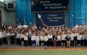 Spolecznosc przedszkolna w strojach galowych podczas spiewania hymnu panstwowego.